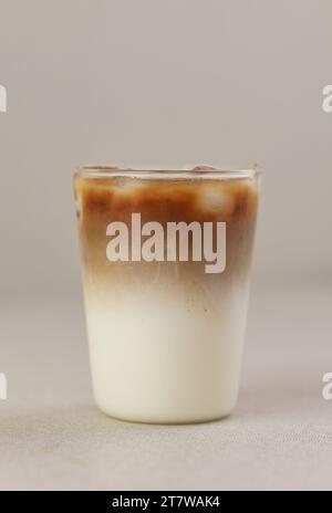 Eiskaffee Latte auf cremefarbenem Hintergrund, Espresso, der mit Eiswürfel in die Milch gießt Stockfoto