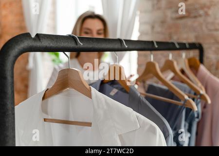 Die Frau durchsucht ihre verschiedenen Outfits, die an der Kleiderstange in ihrem Kleiderschrank hängen Stockfoto