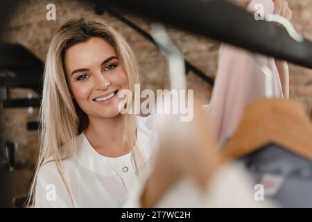 Happy Woman durchstöbert ihre verschiedenen Outfits, die am Kleiderständer in ihrer Garderobe hängen Stockfoto