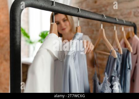 Die Frau durchsucht ihre verschiedenen Outfits, die an der Kleiderstange in ihrem Kleiderschrank hängen Stockfoto