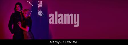 Cosplay-Studenten in Uniform im Neonlicht vor violettem Hintergrund mit Hieroglyphenprojektion, Banner Stockfoto