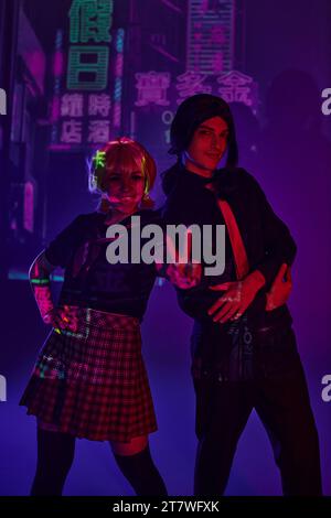 Anime-Frau in Schuluniform mit Siegeszeichen in der Nähe des Mannes auf lila Neon Hintergrund mit Hieroglyphen Stockfoto