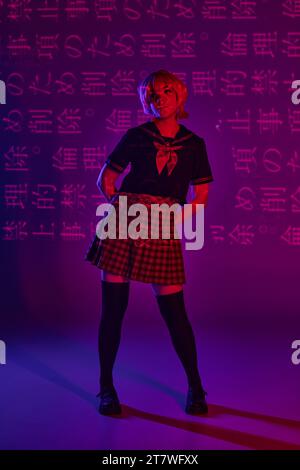 Junge Frau posiert in Schuluniform auf neonviolettem Hintergrund mit Hieroglyphen, Anime-Stil Stockfoto