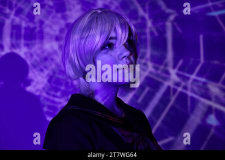 Porträt einer jungen Anime-Stil-Frau in blonder Perücke in blauem Neonlicht auf abstraktem Hintergrund, Cosplay Stockfoto