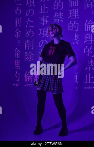 Anime-Style-Frau in Schuluniform mit Hand auf Hüfte in blauem Neonlicht mit Hieroglyphenprojektion Stockfoto