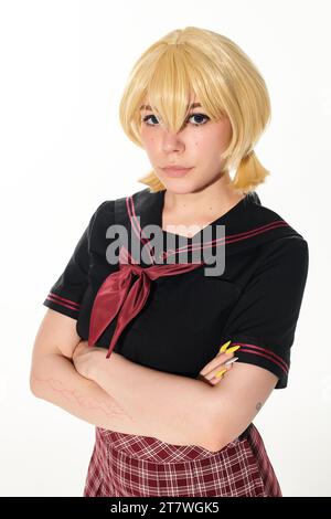 Porträt einer jungen Frau in gelber blonder Perücke und Schuluniform mit Blick auf die Kamera auf weißem Cosplay Stockfoto