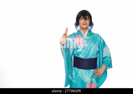 Junger kreativer Mann in blauem Kimono und Perücke, der mit dem Finger auf die Kamera zeigt, auf weiße Cosplay-Kultur Stockfoto