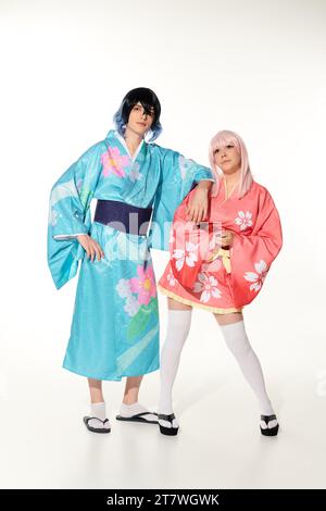 Voller Länge von jungen und lebendigen Paaren in Kimonos und Perücken auf weißer, asiatischer Cosplay-Subkultur Stockfoto