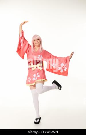 Fröhliche Frau im Anime-Stil in lebendiger traditioneller Kleidung posiert in weißer, japanischer Cosplay-Kultur Stockfoto