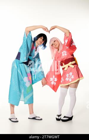 Romantische Cosplayer in Perücken und hellen Kimonos mit großem Herzzeichen und weißen Händen Stockfoto