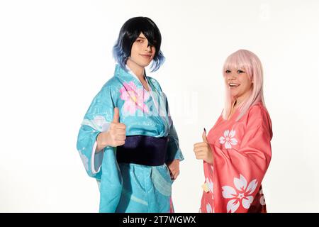 Anime-Paar in Perücken und Kimonos mit Daumen nach oben und Blick auf die Kamera auf weiß, Cosplay-Trend Stockfoto