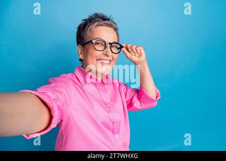 Foto einer optimistischen positiven Frau mit kurzer Frisur gekleideter rosa Bluse, die Selfie-Brille auf blauem Hintergrund macht Stockfoto