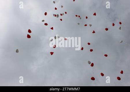Rote und weiße, herzförmige Ballons fliegen am Himmel Stockfoto