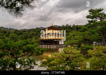 Kinkakuji spiegelt sich auf einem ruhigen Teich, umgeben von üppigem Grün unter einem bewölkten Himmel. Stockfoto