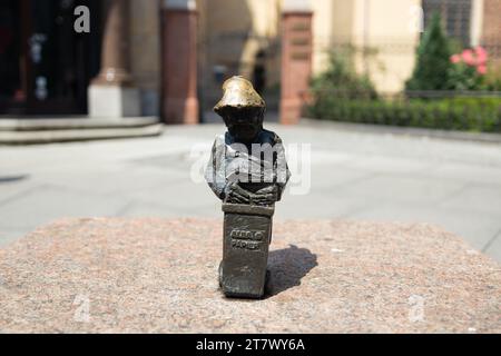 Frau, die eine kleine Zwergstatue auf dem Marktplatz in Breslau berührt. Berühmte kleine Statuen Stockfoto