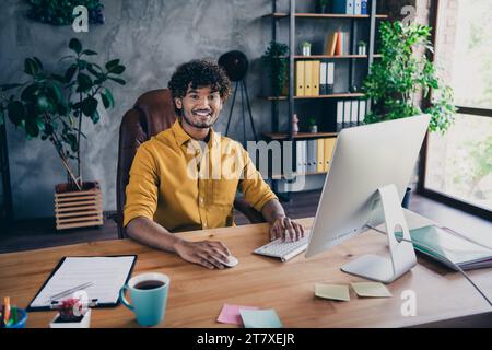 Foto-Porträt des hübschen jungen Mannes tragen gelbes Hemd fröhliches Startup Administrator Arbeitsplatz stilvoller Raum Innenraum Home Office Design Stockfoto