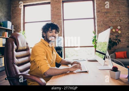 Foto-Porträt des gutaussehenden jungen Mannes tragen gelbes Hemd fröhlich Remote Working Arbeitsplatz Sit Tisch stilvolle Raum Innenraum Home Office Design Stockfoto