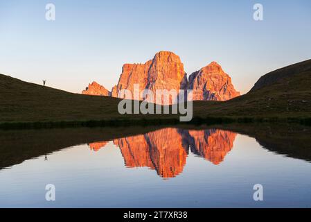 Der Wanderer bewundert den Sonnenuntergang vor dem riesigen Massiv des Pelmo Berges, der sich im Wasser des kleinen Sees von Baste spiegelt Stockfoto