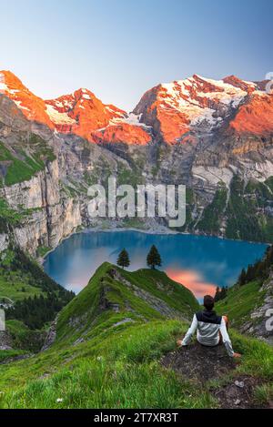 Blick auf einen Wanderer vor dem Oeschinensee, umgeben von einem verschneiten Gipfel bei Sonnenuntergang, Oeschinensee, Kandersteg, Kanton Bern, Schweiz Stockfoto