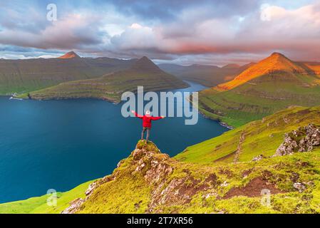 Glücklicher Wanderer steht auf der Klippe mit Blick auf den Fjord von Funningur, Eysturoy Island, Färöer Inseln, Dänemark, Europa Stockfoto