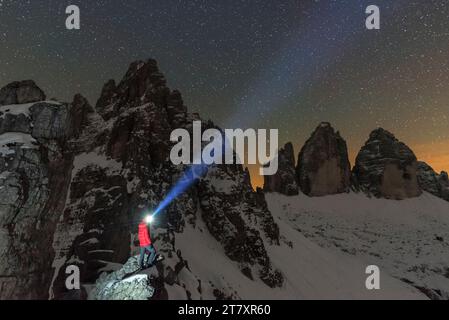 Der Mann mit Stirnlampe beleuchtet den Sternenhimmel über dem verschneiten Paterno und den drei Zinnen von Lavaredo, Sexten und Dolomiten Stockfoto