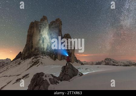 Wanderer mit Taschenlampe Blick auf die drei Zinnen di Lavaredo in einer sternenklaren Nacht mit der Milchstraße, Blick auf den Winter, drei Zinnen di Lavaredo (Lavaredo Gipfel) Stockfoto