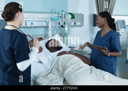 Verschiedene Ärztinnen und männliche Patientin liegen im Bett und reden im Krankenhauszimmer Stockfoto