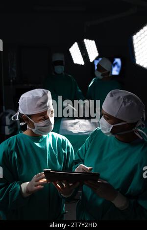 Diverse Chirurgeninnen diskutieren Arbeit mit Tablette im Operationssaal im Krankenhaus Stockfoto