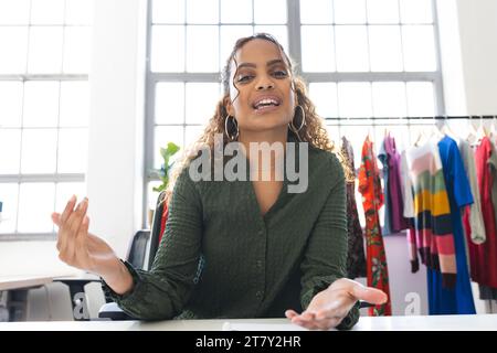 Glückliche, birassische Modedesignerin, die Videoanrufe am Schreibtisch im Studio hat Stockfoto