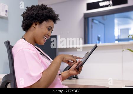 Glückliche afroamerikanische Ärztin mit Tablette im Krankenhausempfang Stockfoto