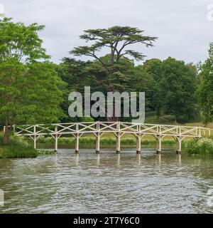 Blick auf die Chinesische Brücke über den Serpentine Lake mit der Great Cedar Tree dahinter im Painshill Park, Cobham, Surrey, England, Großbritannien. Stockfoto