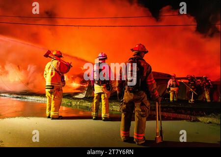 Feuerwehrmänner im Kampf gegen eine spektakuläre Flamme auf dem RK Miles Holzlager in Montpelier, VT, New England, USA. Stockfoto