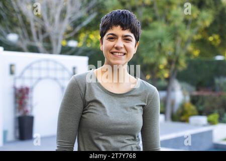 Porträt einer glücklichen birassischen Frau mit kurzen dunklen Haaren, die lächelnd auf der Gartenterrasse steht Stockfoto