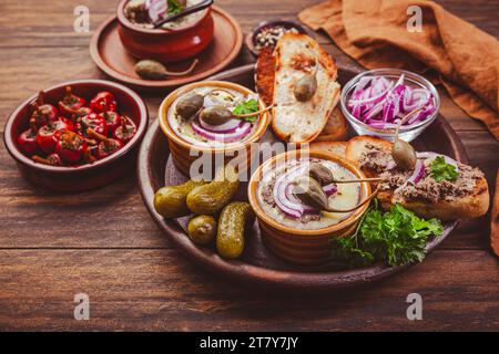 Frische hausgemachte Hühnerleber-Pastete in Keramikschalen und Vorspeisen auf rustikalem Hintergrund Stockfoto