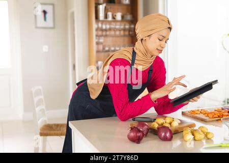 Birassische Frau in Hijab und Schürze mit Tablette in der Küche Stockfoto