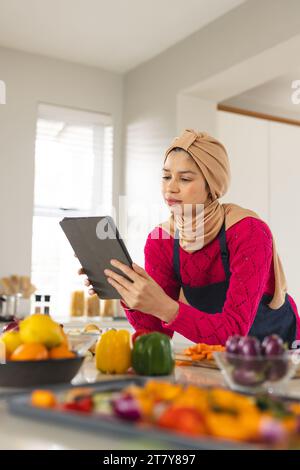 Birassische Frau in Hijab und Schürze mit Tablette in der Küche Stockfoto