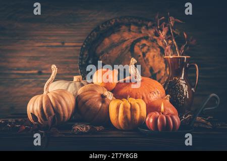 Stillleben im Herbst mit Kürbissen und Kerzen auf hölzernem Hintergrund. Thanksgiving Wohndekoration. Stockfoto