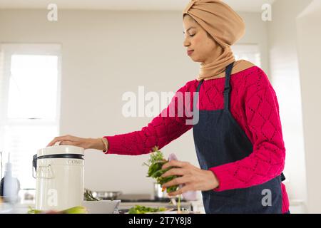 Birassische Frau in Hijab und Schürze, die Gemüseabfälle in der Küche kompostiert Stockfoto