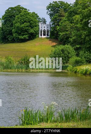 Blick auf den gotischen Tempel auf einem Hügel hinter dem Serpentine Lake im Painshill Park, Cobham, Surrey, England, Großbritannien. Stockfoto