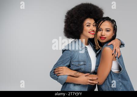 Fröhliche und trendige afroamerikanische Freundinnen mit grauem Hintergrund, Denim-Mode Stockfoto