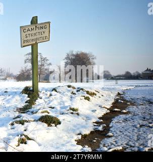 1960er Jahre, im Winter und neben einem Pfad in einem Park, mit Schnee auf dem Boden, ein hölzernes Schild mit der Aufschrift „Camping strikt verboten“, England, Großbritannien. Stockfoto