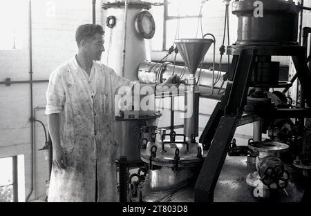 1960er Jahre, historisch, ein männlicher Agent, in schmutzigen Arbeitsanzügen, auf einer hohen Plattform stehend, an der Ausrüstung einer Lackierfabrik in England, Großbritannien. Stockfoto