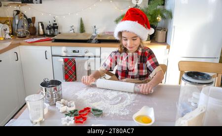 Tochter lernt kochen, rollt den Teig mit einer Nudelnadel aus, hilft in der weißen Küche und Kekse für Weihnachten und Neujahr. Stockfoto