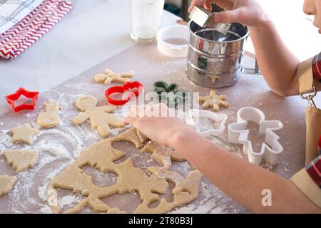 Die Hände von mutter und Tochter schneiden Kekse aus dem Teig heraus, mit Schimmelpilzen auf einem Weihnachtsmotiv in Form eines Schneemanns, eines Weihnachtsbaums, Sterns Stockfoto