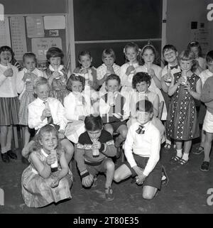 1965, historisch, eine Gruppe von Grundschulkindern, die ihre kleinen Flaschen (200 ml) Morgenmik trinken. Schulkinder in der Grund- und Sekundarschule erhielten morgens Milch als Ernährungsvorteil und vor dem Mittagessen zur Hydration, da nach der großen Depression und zwei Weltkriegen die Unterernährung von Kinderhunden bekämpft werden musste. Sie begann 1946, wurde in den späten 60er Jahren für weiterführende Schulen und dann 1971 für Kinder über sieben Jahren beendet. Stockfoto