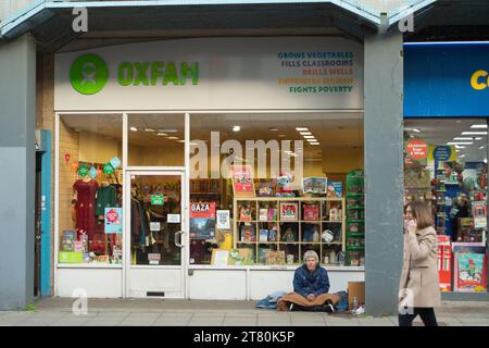 Uxbridge, Großbritannien. November 2023. Ein Obdachloser sitzt vor einem Oxfam Charity Shop im Stadtzentrum von Uxbridge im Londoner Stadtteil Hillingdon. Die Pläne der ehemaligen Innenministerin Suella Braverman, keine Wohltätigkeitsorganisationen mehr an Obdachlose zu vergeben, wurden von der Regierung aufgegeben. Quelle: Maureen McLean/Alamy Live News Stockfoto