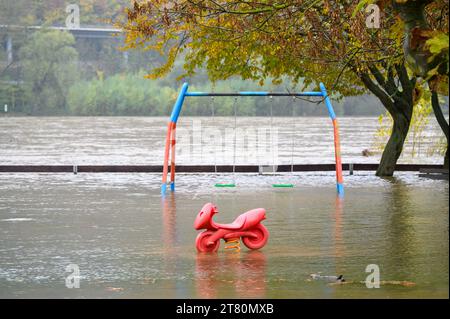 Ein Spielplatz wird nach sintflutartigen Regenfällen überflutet, was dazu führt, dass der benachbarte Fluss über seine Ufer bricht und eine Schaukel und ein Motorrad sitzen auf federndem Spielzeug Stockfoto