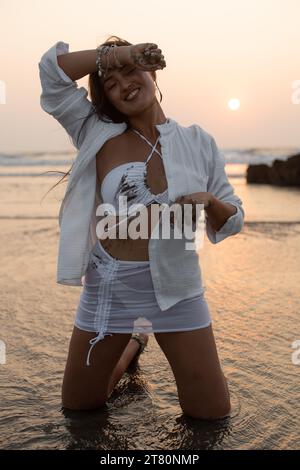 Porträt einer jungen zufriedenen asiatischen hübschen Frau, die nass schmutzigen weißen Badeanzug trägt, Hemdrock, der auf Knien im Wasser steht. Stockfoto