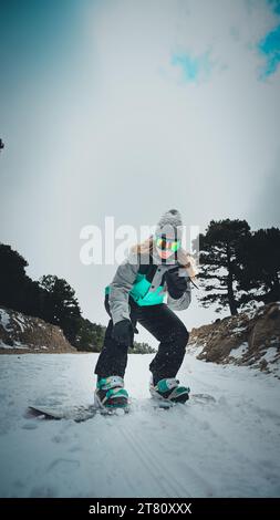 Eine fröhliche junge Snowboarderin gleitet einen winterlichen Berghang hinunter, umgeben von einer Decke aus unberührtem weißem Schnee Stockfoto