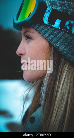 Eine Frau mit marineblauer Wintermütze und dazu passender, grün getönter Brille steht vor weißem Hintergrund und blickt zur Seite Stockfoto